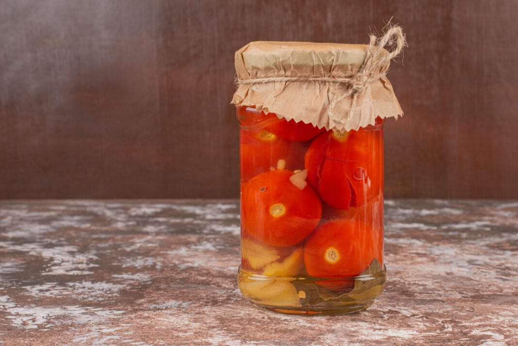 Jar of homemade pickled tomatoes on marble table